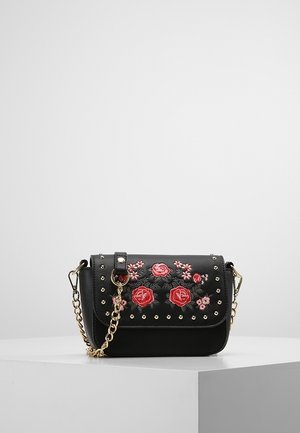 Schwarze Crossbody-Tasche mit goldener Kettenriemen, roter und rosa floraler Stickerei und goldenen Nieten auf weißer Oberfläche.