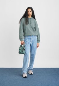 Groene hoodie, blauwe verticaal gestreepte jeans, grijze sneakers, met een kleine groene tas. Eenvoudig ontwerp met een relaxte pasvorm.