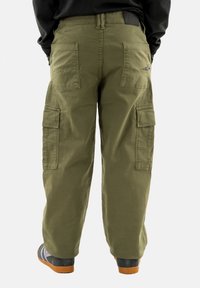 Pantaloni cargo verde oliva con molte tasche e una vestibilità rilassata. Tessuto resistente con superficie texturizzata. Presenta un patch con logo in vita.