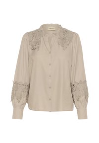 Blouse beige clair avec un col à volants, fermeture à boutons sur le devant et des accents de dentelle complexes sur les épaules et les manches. Texture de tissu lisse.