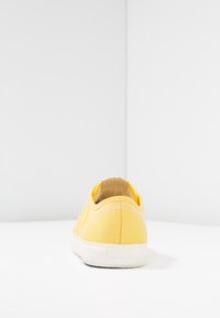 Gul canvas sneakers med rundad baksida, kontrasterande vit sömnad och vit gummistropp. Har en liten GANT-logotyp på hälen.