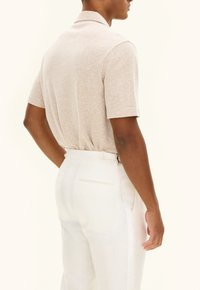 Beige kortärmad polo skjorta med strukturerad tyg, bärs med vita byxor. Skjortan har en lätt lyster och en klassisk kragsdesign.