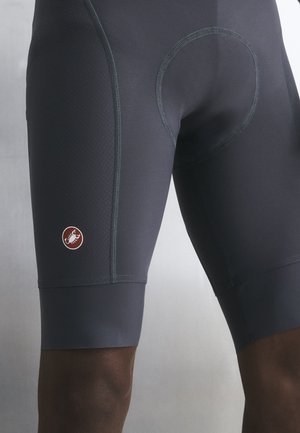 Prikaz tamnosivih uteznih biciklističkih hlačica nošenih na gornjem dijelu nogu, s malim okruglim logotipom na lijevom bedru.