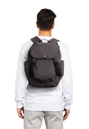 Sac à dos en tissu gris avec une fermeture à rabat, des bretelles réglables et des poches latérales, présentant un design simple et peu de détails matériels.