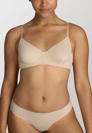 Donna che indossa un completino abbinato color nudo, composto da reggiseno e slip, mostrata dal collo fino alla parte superiore delle cosce su uno sfondo chiaro e uniforme.