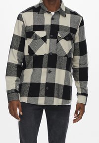 Czarna i biała koszula flanelowa w kratę z dwoma kieszeniami na piersi, zapinana na guziki z klasycznym kołnierzykiem, wykonana z miękkiego, teksturowanego materiału.