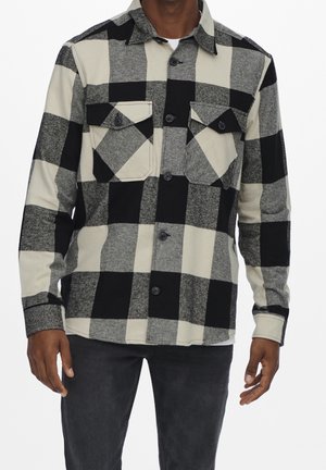 Chemise en flanelle à carreaux noir et blanc avec deux poches poitrine, boutonnière à l'avant et col classique, dotée d'un tissu doux et texturé.
