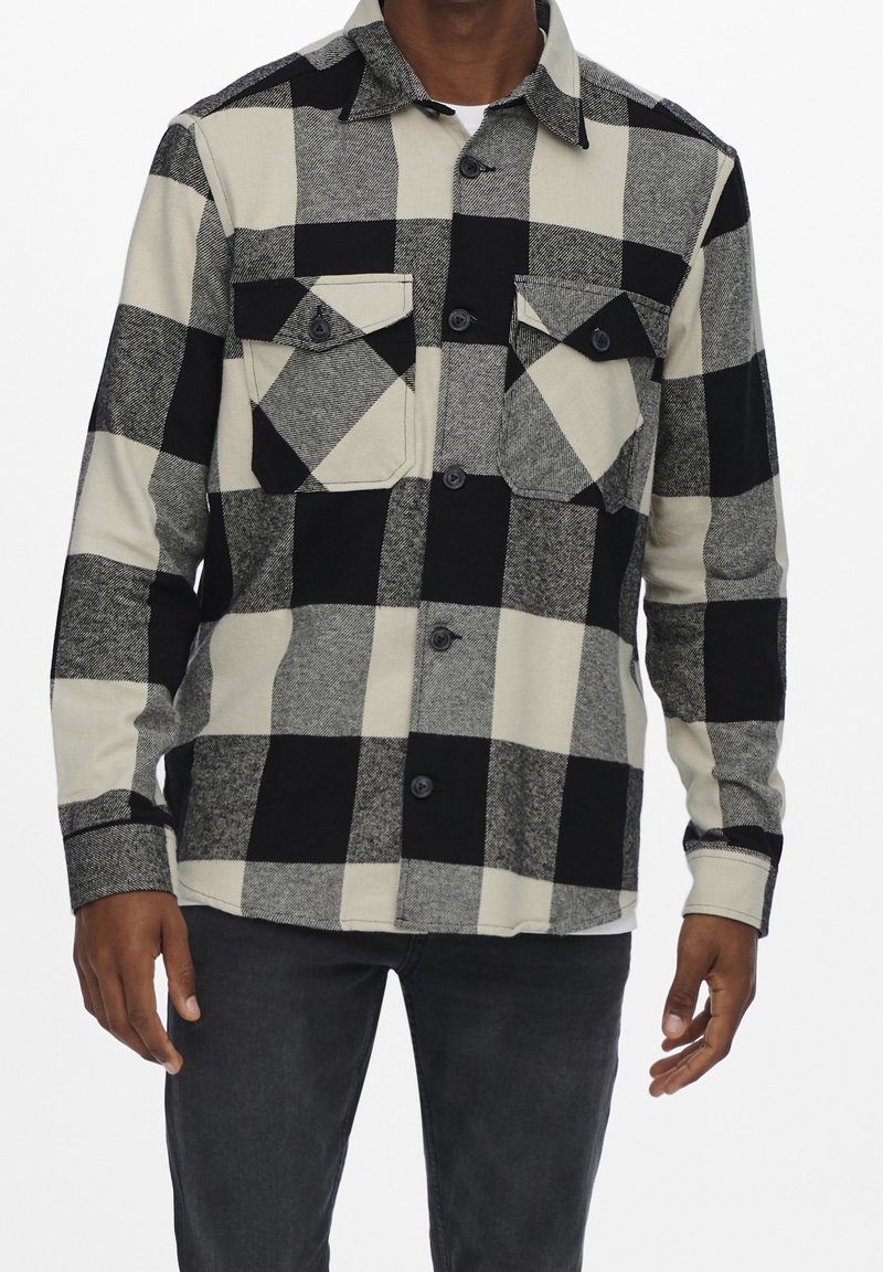 Czarna i biała koszula flanelowa w kratę z dwoma kieszeniami na piersi, zapinana na guziki z klasycznym kołnierzykiem, wykonana z miękkiego, teksturowanego materiału.