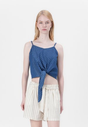 Top corto in denim blu con dettaglio ancorato sul davanti e spalline sottili, abbinato a pantaloni corti bianchi a righe con vita regolabile.