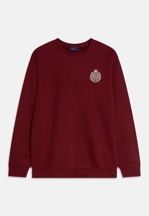 Sweatshirt bordeaux en tissu doux, avec un col rond, des manches longues et un petit logo blanc sur la poitrine.
