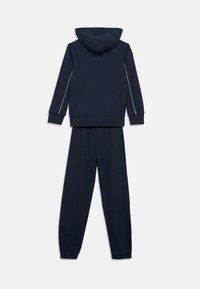 Ναυτικό μπλε φούτερ με κουκούλα και λευκές ρίγες στα πλάγια, συνοδευόμενο από αντίστοιχο παντελόνι φόρμας. Και τα δύο είναι κατασκευασμένα από απαλό ύφασμα με ελαστικές μανσέτες και μέση.