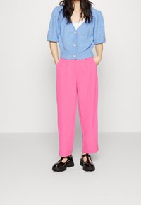 Light blue knitted cardigan with short puff sleeves and button closure, paired with high-waisted pink trousers and black platform shoes.