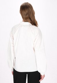 Hvid skjorte med knapper og puffede ærmer, der har en struktureret krave og en samlet rygdesign. Glat tekstur, ingen synlige mønstre.