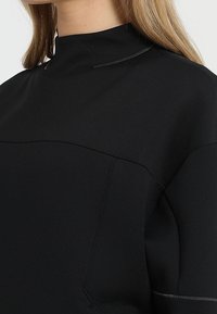 Svart tröja med hög hals, med en strukturerad tyg, insydda sömmar och kontrasterande sömnadsdetaljer för extra dimension.