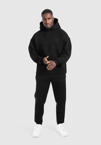 Set di felpa con cappuccio e pantaloni della tuta neri realizzato in tessuto morbido, con stampa in rilievo del logo e una vestibilità rilassata, abbinato a sneakers bianche.
