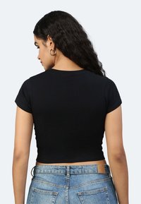 Maglietta nera corta con maniche corte e scollo rotondo, realizzata in un tessuto morbido, abbinata a jeans blu a vita alta.