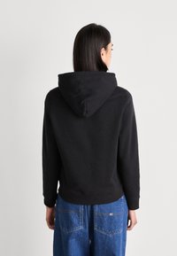 Sudadera con capucha negra de corte holgado, fabricada en algodón, con puños acanalados. Presenta una costura en la parte posterior y un diseño sencillo, sin adornos.