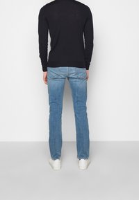 Maglietta nera a maniche lunghe abbinata a jeans dritti blu chiari e sneakers bianche. La maglietta presenta una texture semplice e liscia.