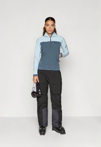 Giacca da sci blu e grigia con zip frontale, abbinata a pantaloni da sci neri con tasche laterali e dettagli grigi. Include occhiali da sci.