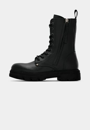 Zwarte leren combatboot met dikke zool, vetersluiting aan de voorkant, ritssluiting aan de zijkant en een trekhaak aan de achterkant, weergegeven vanuit de buitenkant.