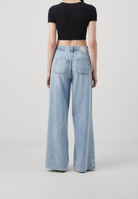 Vaaleansinisiä leveälahkeisia farkkuja, joissa on korkea vyötärö. Ne sisältävät kaksi takataskua ja pienen logopatchin, ja ne on valmistettu haalistuneesta denim-kankaasta.
