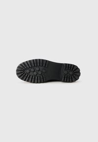 Black rubber shoe outsole with a textured surface featuring hexagonal and herringbone patterns for enhanced grip.