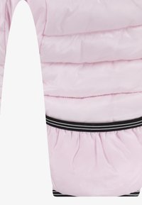 Pufīgs rozā jakas ar horizontālu quilted sadaļu. Raksturīga melnbalta elastīga jostasvieta un gluda, spīdīga auduma tekstūra.