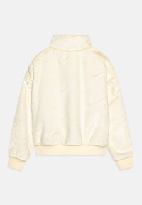 Kremowy polar Nike o miękkiej, teksturowanej tkaninie, z wysokim kołnierzem i prążkowanymi mankietami; posiada wytłoczony wzór z logo Nike na całej powierzchni.