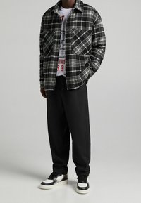 Köksrutig svart och vit flanelljacka, grå T-shirt med grafik, svarta avslappnade byxor och svartvita sneakers.