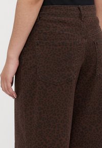 Bruine luipaardprint broek van een textuurstof. Voorzien van twee achterzakken en een aansluitende tailleband. Zichtbare stiksels benadrukken het ontwerp.