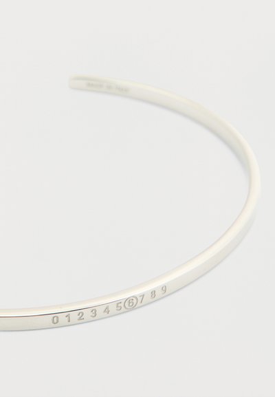 Λεπτό ασημένιο βραχιόλι με χαραγμένους αριθμούς από το 0 έως το 9, ο αριθμός 6 είναι κυκλωμένος, σε λευκό φόντο.