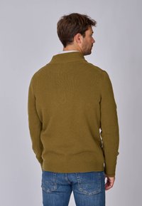 Pull en maille texturée vert olive avec col haut, manches longues et ourlet côtelé. La vue arrière montre un design épuré et une coupe décontractée.