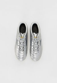 Pantofi de fotbal argintii cu un superior din piele texturată, sireturi plate, guler căptușit și tălpi negre cu un logo. Design cu vârful neted și rotunjit.