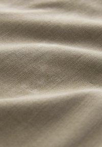 Close-up of soft beige fabric with visible diagonal weave texture and gentle folds creating light and shadow variations.