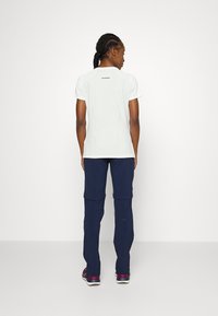 Chemise blanche à manches courtes avec un design ajusté et un logo au dos, associée à un pantalon bleu foncé avec des poignets zippés et des coutures détaillées.