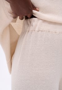 Pull en tricot beige et pantalon assorti avec une finition texturée. Les pantalons présentent une taille élastique. Vue en gros plan du vêtement.