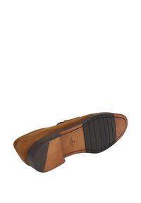 Scarpa in suede marrone con punta rotonda, suola in gomma nera e un piccolo tacco. Cuciture evidenti e accenti in metallo sul tacco.