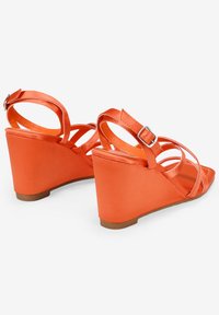 Sandalias de cuña en un vibrante color naranja con un acabado satinado suave. Cuenta con múltiples tiras cruzadas y una hebilla ajustable en el tobillo.