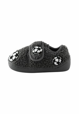 Zapatilla infantil negra con tejido suave y texturizado, cierre de velcro y diseños de balones de fútbol blancos y negros en la parte superior y los laterales.