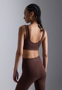 Sostenes deportivos marrones y leggings de cintura alta hechos de una tela elástica, con un escote posterior y un detalle del logotipo en la cinturilla.
