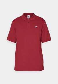 Polo-shirt en coton rouge avec un col, des manches courtes et un logo Nike blanc sur le côté gauche de la poitrine. Texture lisse.