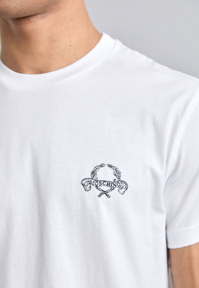 Tricou alb din bumbac, cu un logo brodat negru și accente de lauri, amplasat pe zona stângă a pieptului. Gât clasic de tip crew.