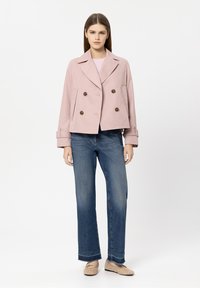 Light pink, double-breasted jacket with large buttons, tailored fit, and side pockets. Paired with blue jeans and beige shoes.