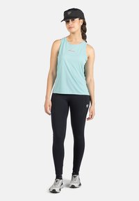 Helles blaues Sport-Top mit figurnaher Passform, kombiniert mit schwarzen Leggings und grauen Laufschuhen. Schwarze Baseballmütze auf dem Kopf.