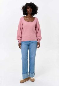 Lichtroze textuursweater met een vierkante halslijn, gecombineerd met lichtblauwe rechte jeans met opgerolde boorden en beige sneakers.