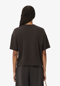 T-shirt nera a maniche corte con vestibilità rilassata, scollatura rotonda e una texture morbida e liscia. Abbinata a pantaloni scuri coordinati.