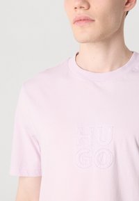 Lyserød bomuld T-shirt med korte ærmer, der har et prægede "HUGO" logo foran, rund halsudskæring og glat tekstur.