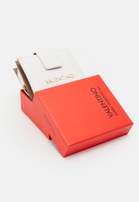 Portefeuille en cuir blanc avec un rabat, logo 'VALENTINO' en relief, à l'intérieur des emplacements pour cartes marron et beige, dans une boîte rouge avec un marquage 'VALENTINO'.