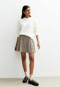 Witte kabelgebreide trui, geruite rok in bruin en beige, zwarte instappers en beige enkelkousen. Eenvoudig en casual outfitontwerp.
