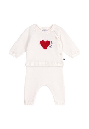 Cremefarbenes gestricktes Babyoutfit mit langen Ärmeln und Hose, mit einem roten Herz und Knöpfen entlang der Schulter und Seite.